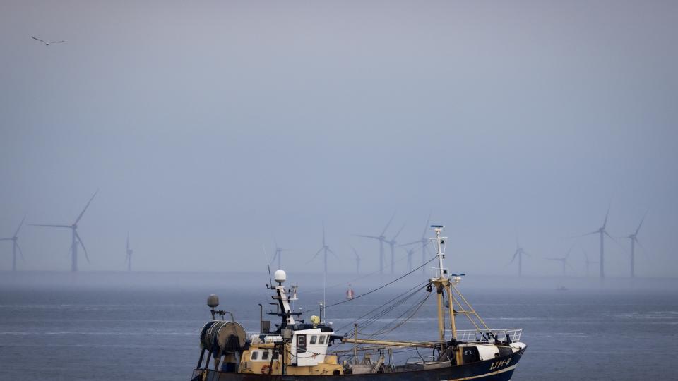 Vissersboot op zee met op de achtergrond windturbines
